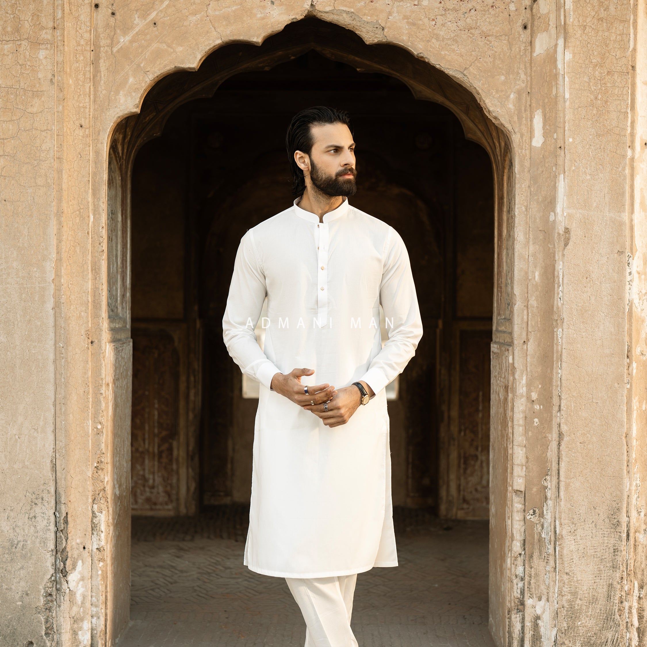Premium white unstitched kurta by Admani Man - Classic menswear shalwar kameez showcased in a traditional Pakistani architectural setting.